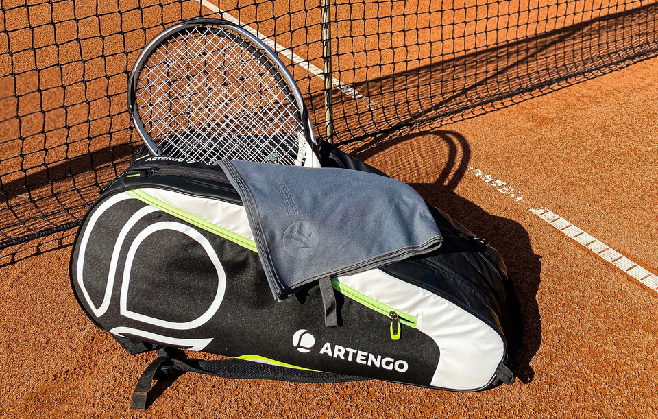 Microfaser-Handtuch liegt auf einer Tennistasche mit Tennisschläger vor einem Netz